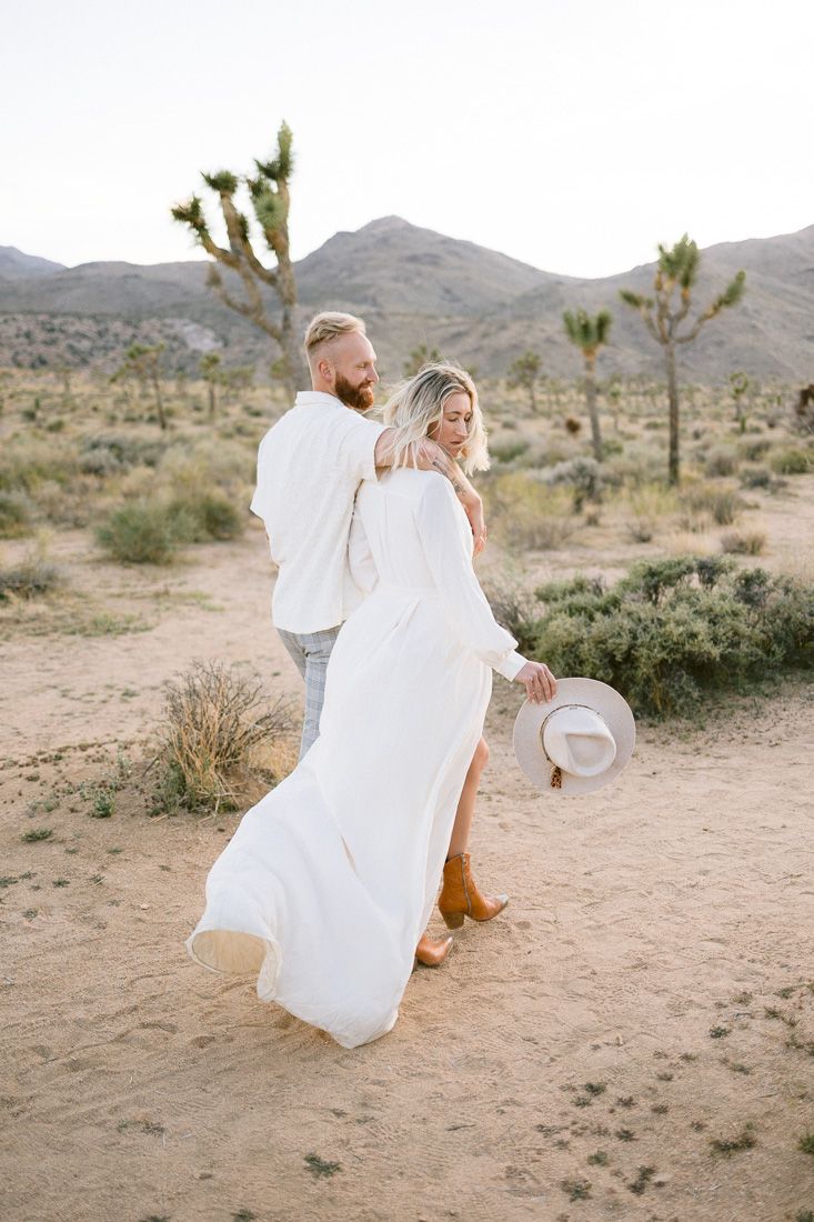 Dancing in white attire among Joshua trees and desert brush with mountains in the distance.