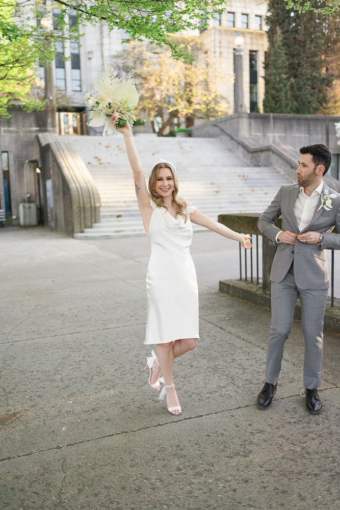 A couple in wedding attire poses playfully on stone steps with the bride twirling in her white dress.