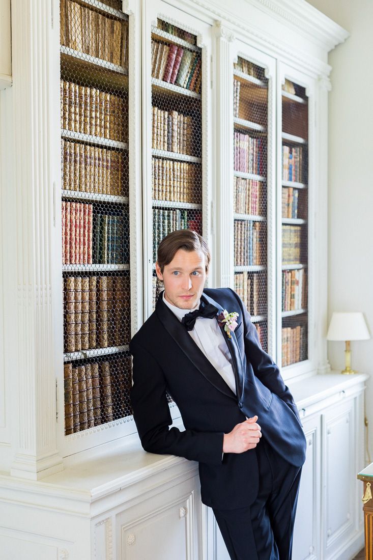 Elegant groom portrait against built-in library bookshelves in formal attire.