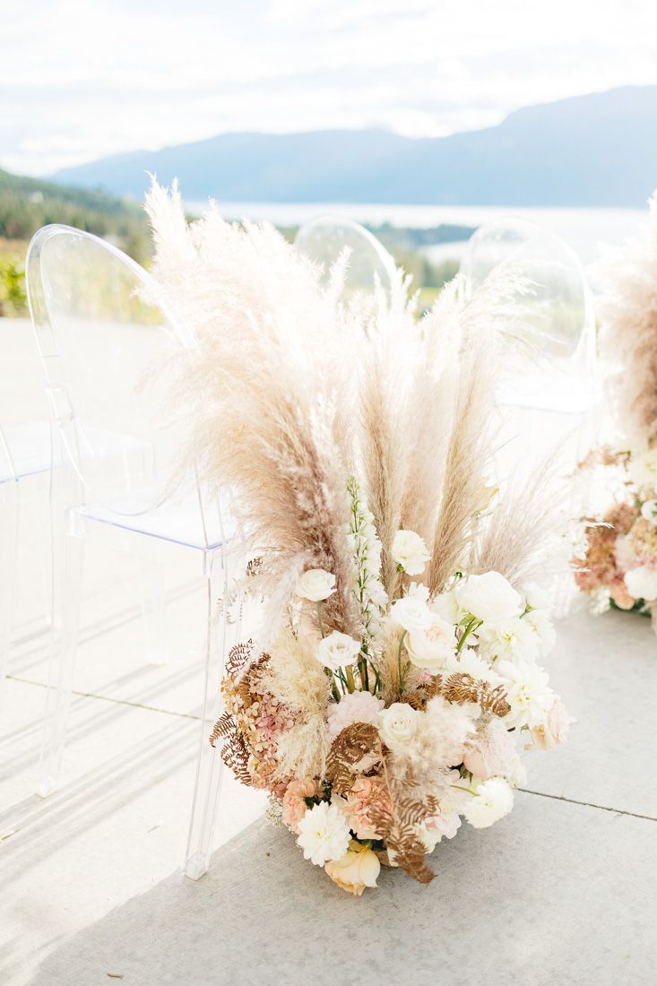 Romantic floral arrangement with pampas grass and white blooms set against mountain landscape.