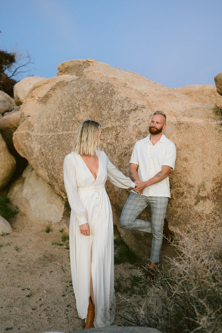 Two people share a moment against a textured rock formation in the desert.