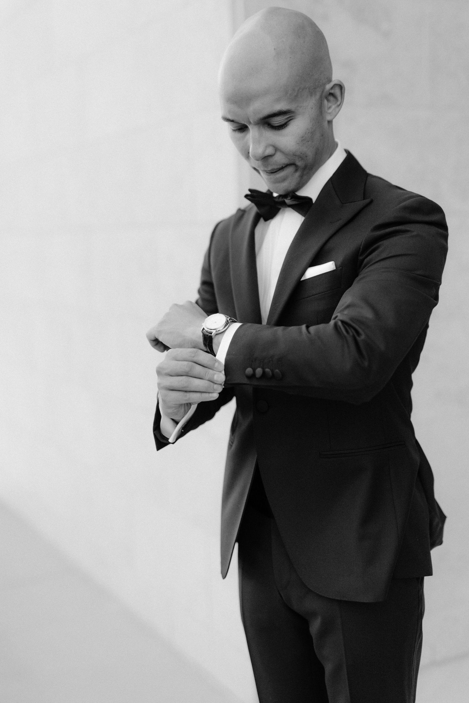 A well-dressed figure in a tuxedo checking their watch in an elegant black and white portrait.