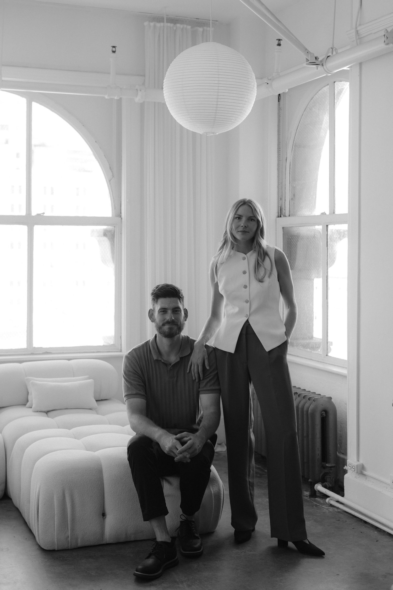 A black and white photo sequence showing a person sitting and moving around a minimalist white room with a bed.