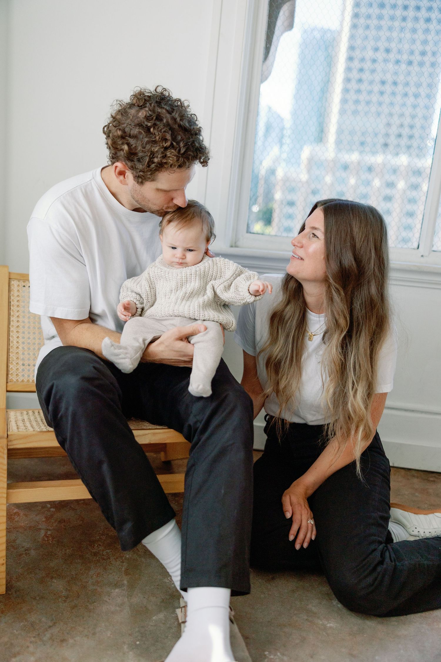Family sharing tender moment together while sitting on wooden bench near window.