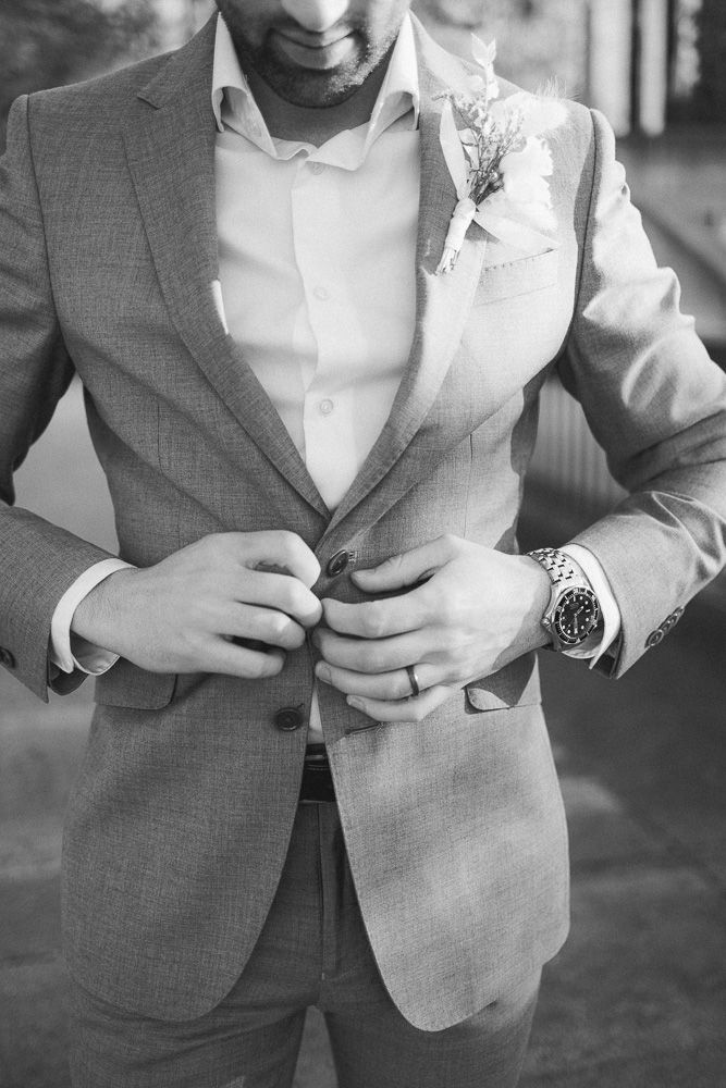 Close-up of a gray suit jacket with boutonniere and watch details.