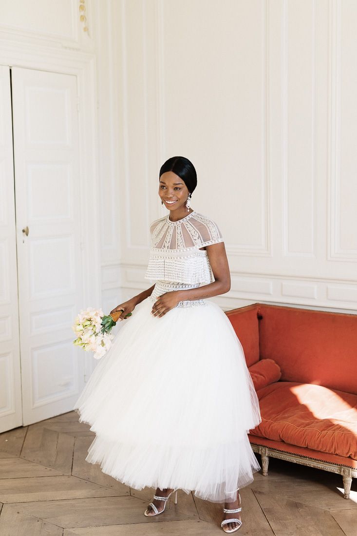 Bride in retro-style tea-length gown smiles while holding white bouquet.