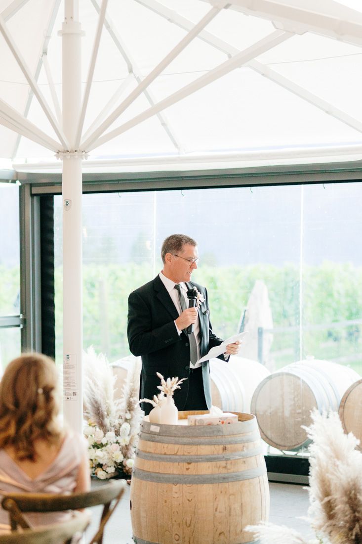 A speaker gives a toast at an elegant wedding reception with wine barrels and pampas grass decor.