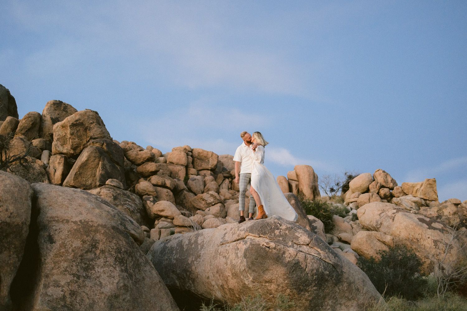 Couple embracing on rocky desert outcrop during golden hour.