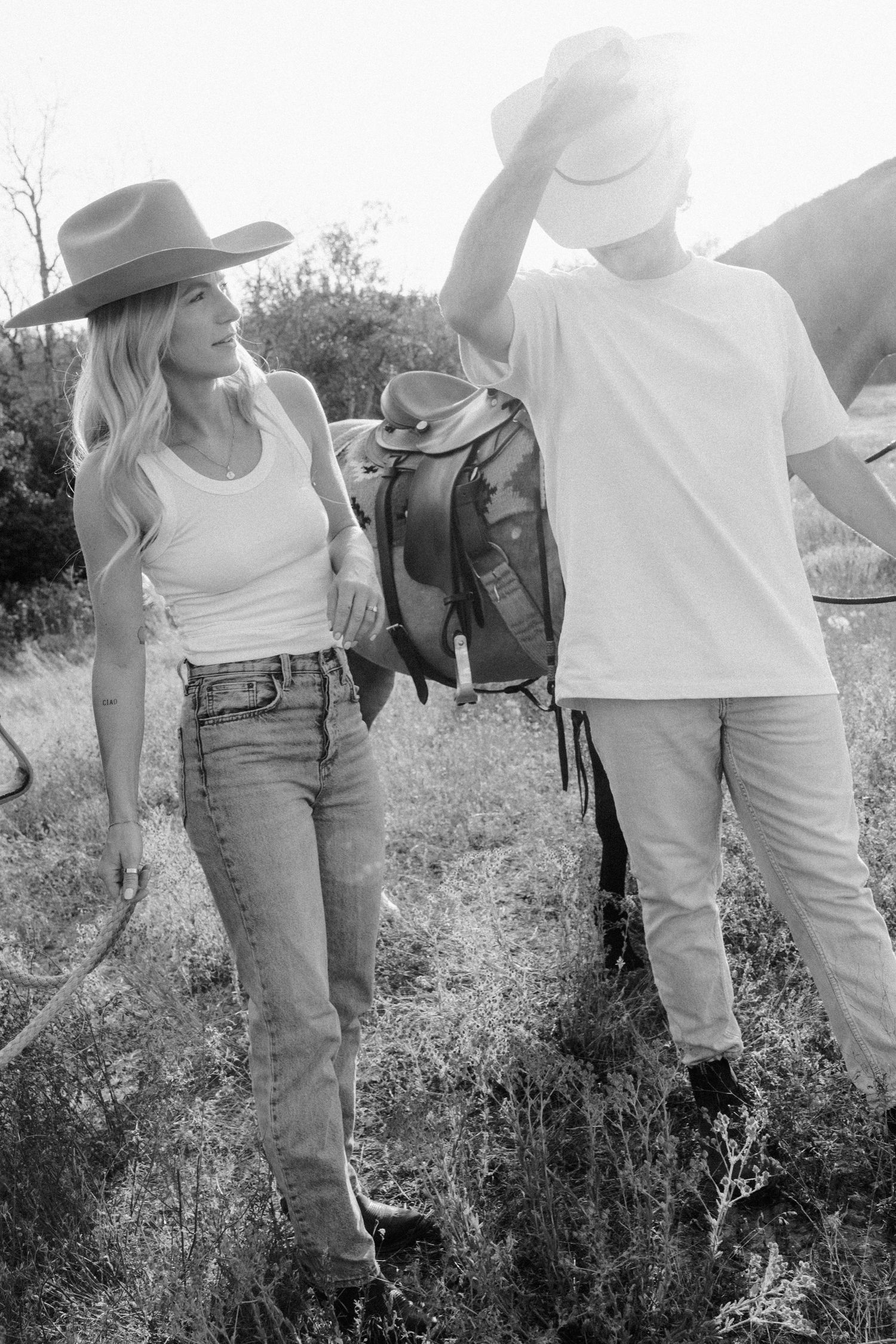 Casual western-style scene with horses and people gathered in a grassy field.