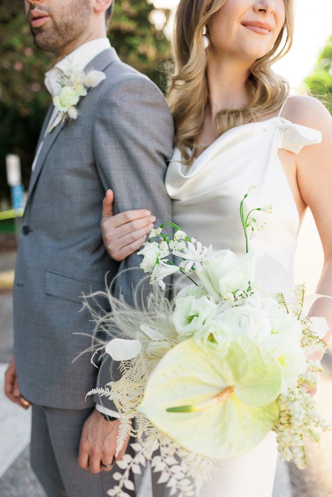 Wedding couple in grey suit and white dress with stunning anthurium and white floral bouquet.