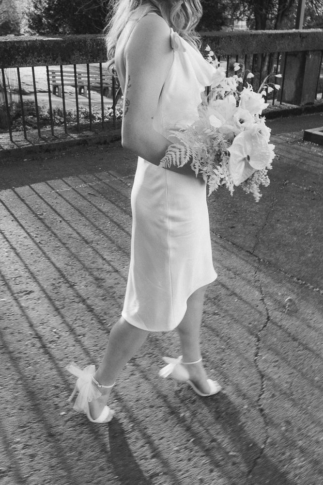 Black and white photo of bride in white dress holding bouquet while walking.