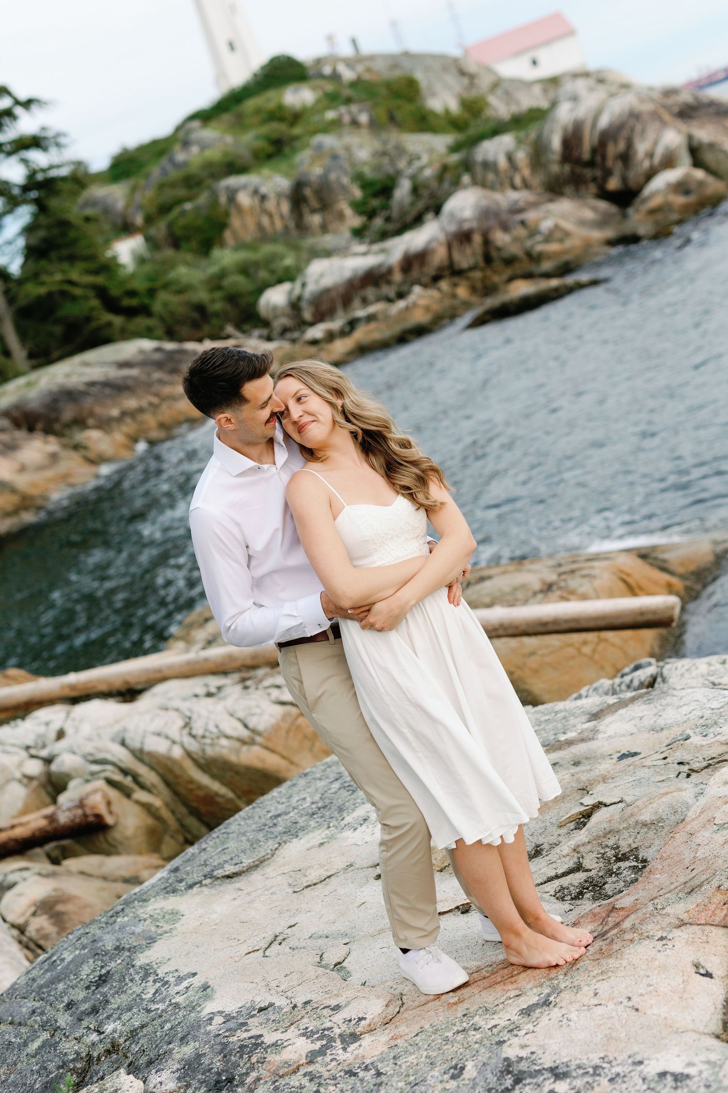 A romantic couple shares an intimate moment on rocky coastal cliffs overlooking the ocean at sunset.