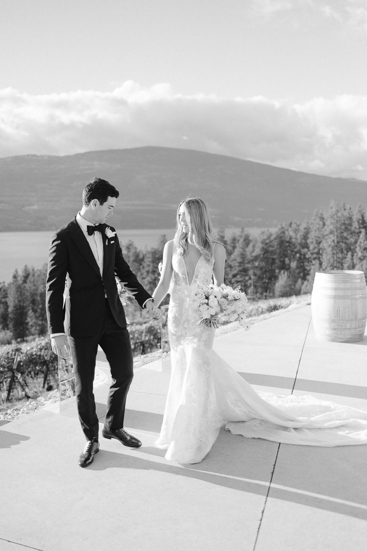 Black and white wedding photo of couple walking on terrace with mountain vista.