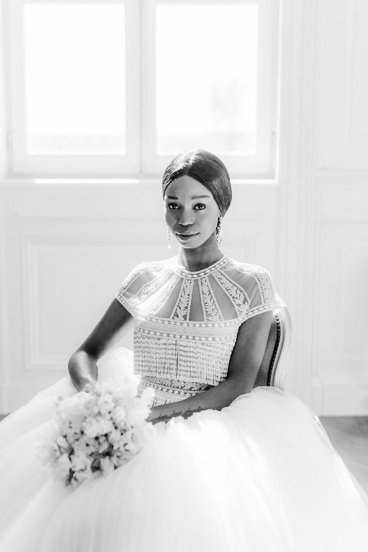 Elegant bridal portrait in white lace gown with high neckline and floral bouquet in black and white.