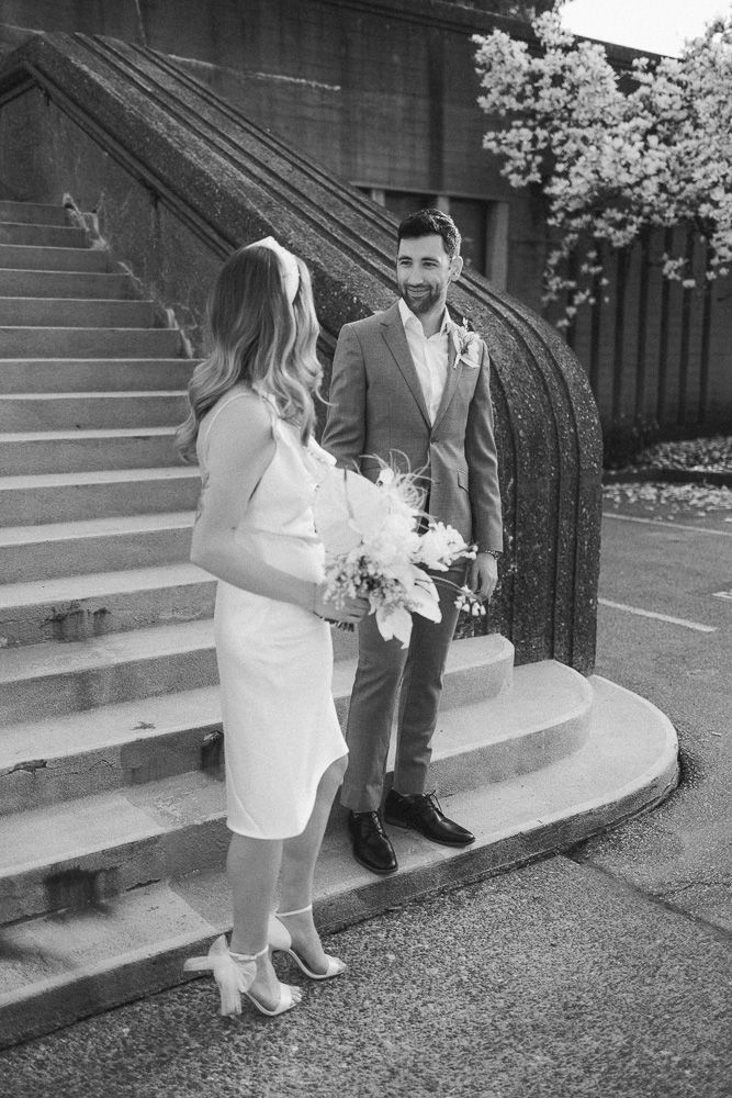 A black and white wedding photo of a couple on stone steps with classic architecture.