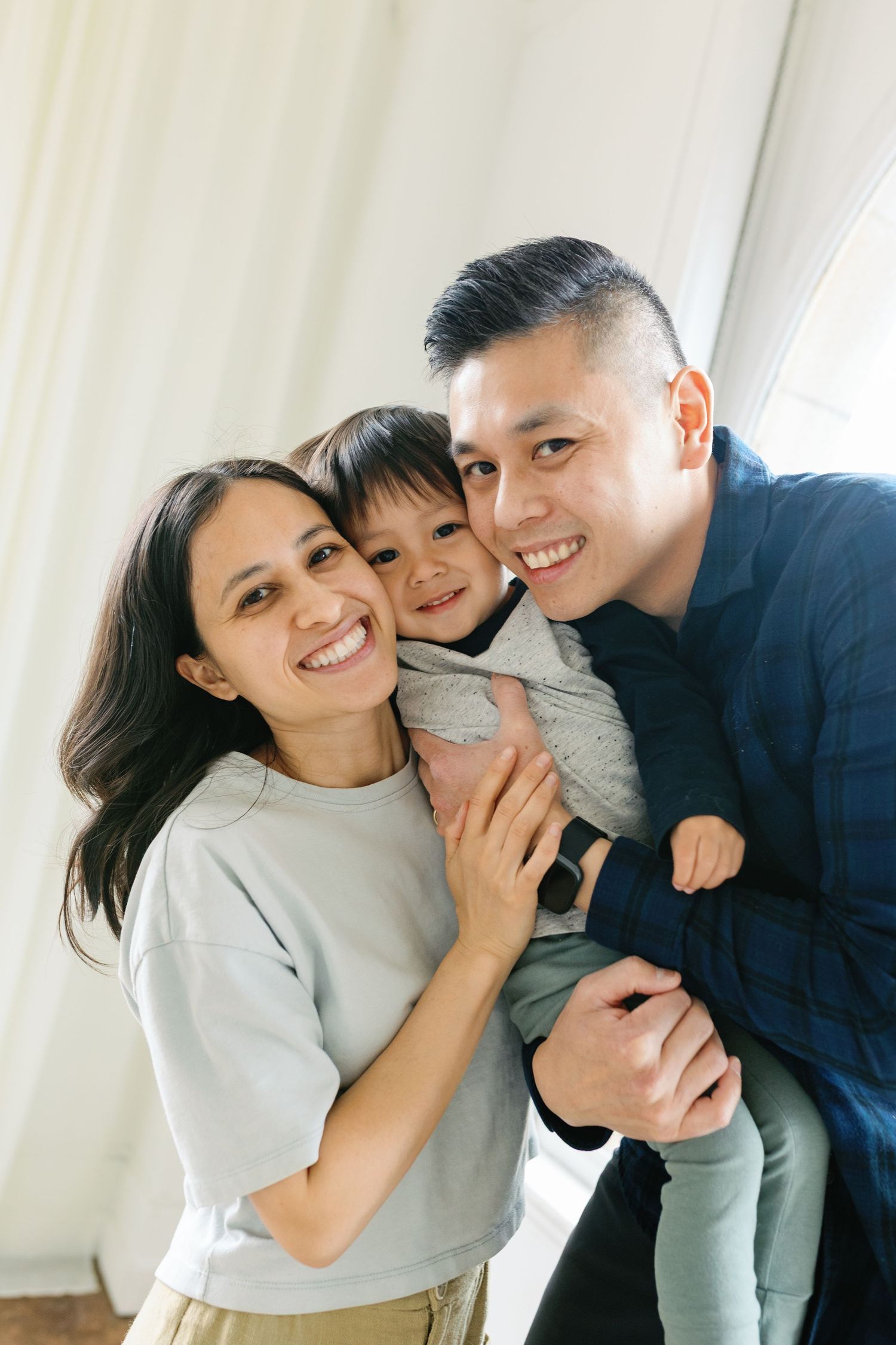 Family poses together playfully in white and gray casual outfits against bright interior wall.