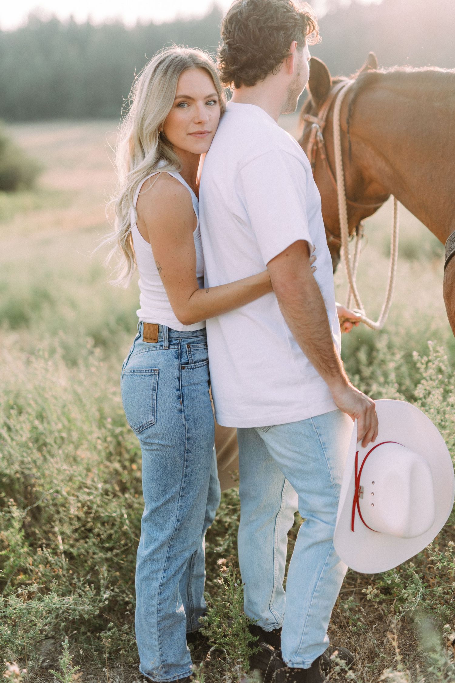 A couple in casual attire shares tender moments in a sun-drenched meadow with their horse.