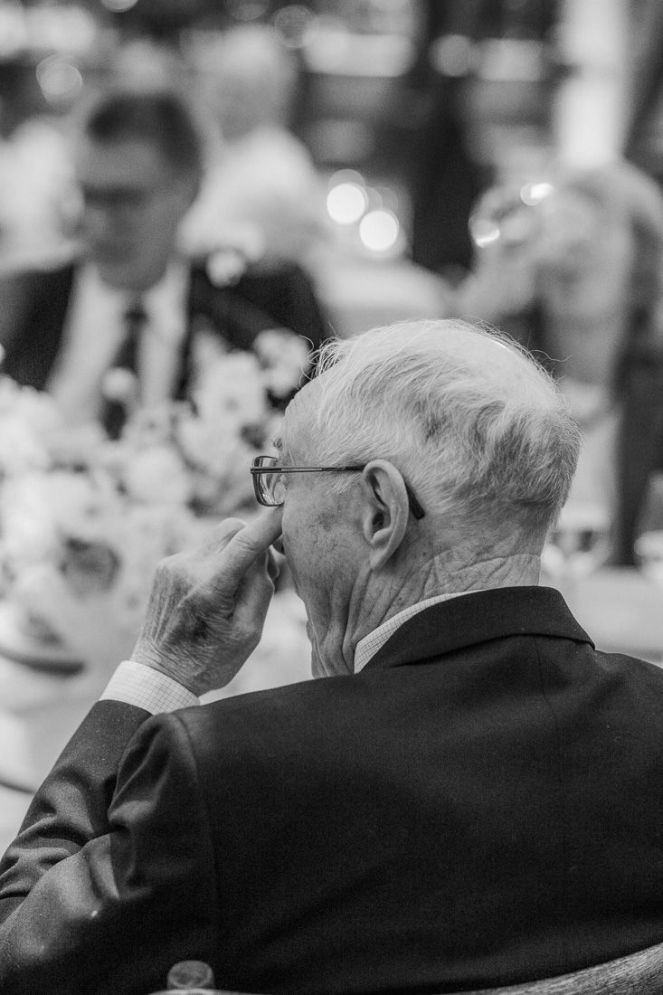 A black and white candid photo of an elderly guest in a suit at a wedding reception.