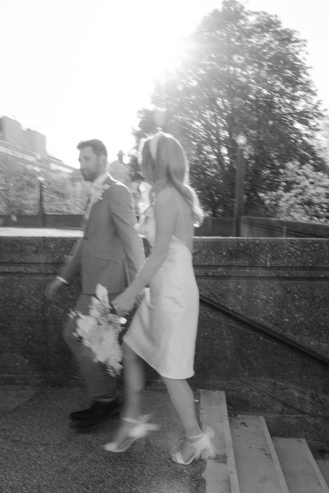 Black and white photo of a couple climbing stairs outdoors in wedding attire.