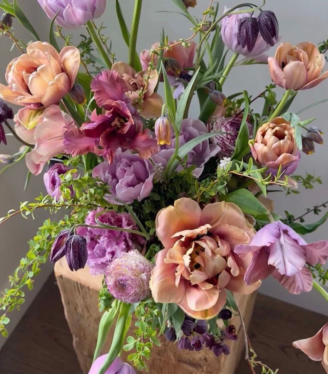 Elegant floral arrangement featuring peach and purple blooms with delicate greenery in a rustic stone vase.