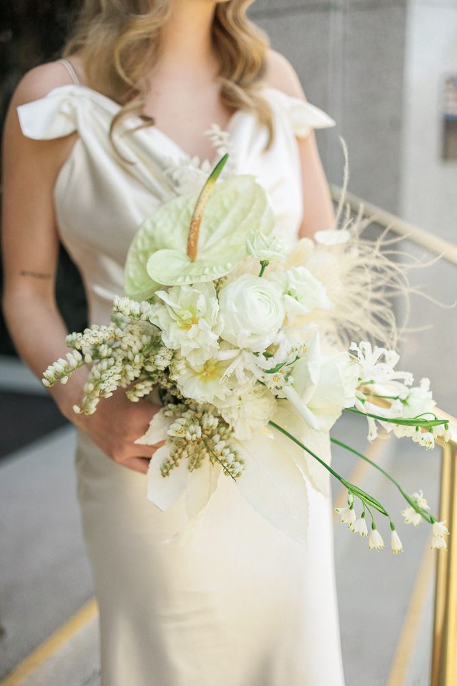 Elegant white and green wedding bouquet with feather accents held against a white dress.