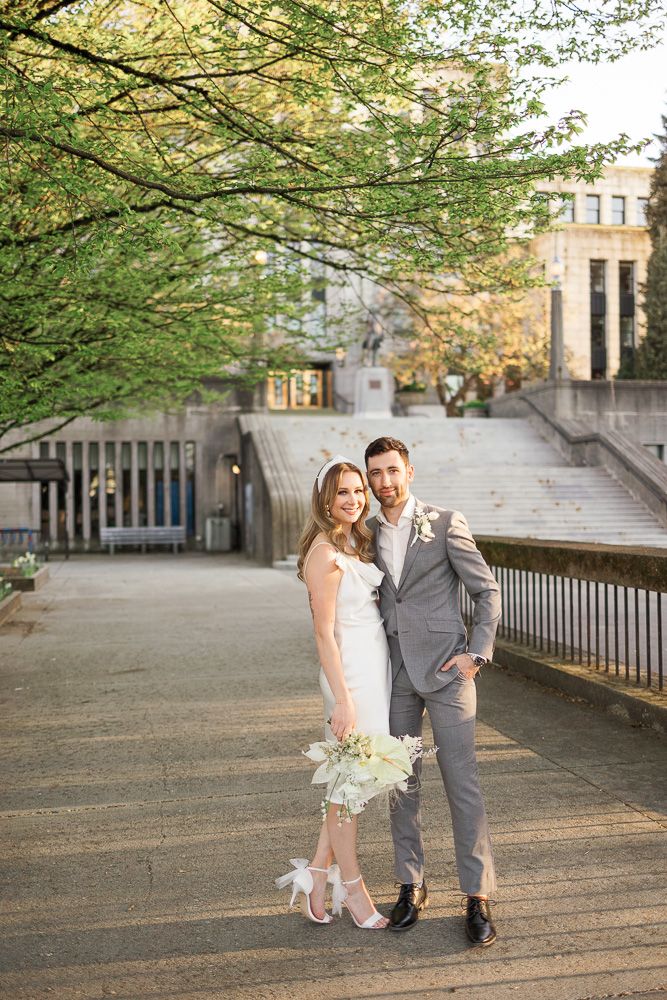 Wedding couple smiling together outdoors with architectural steps and greenery behind them.