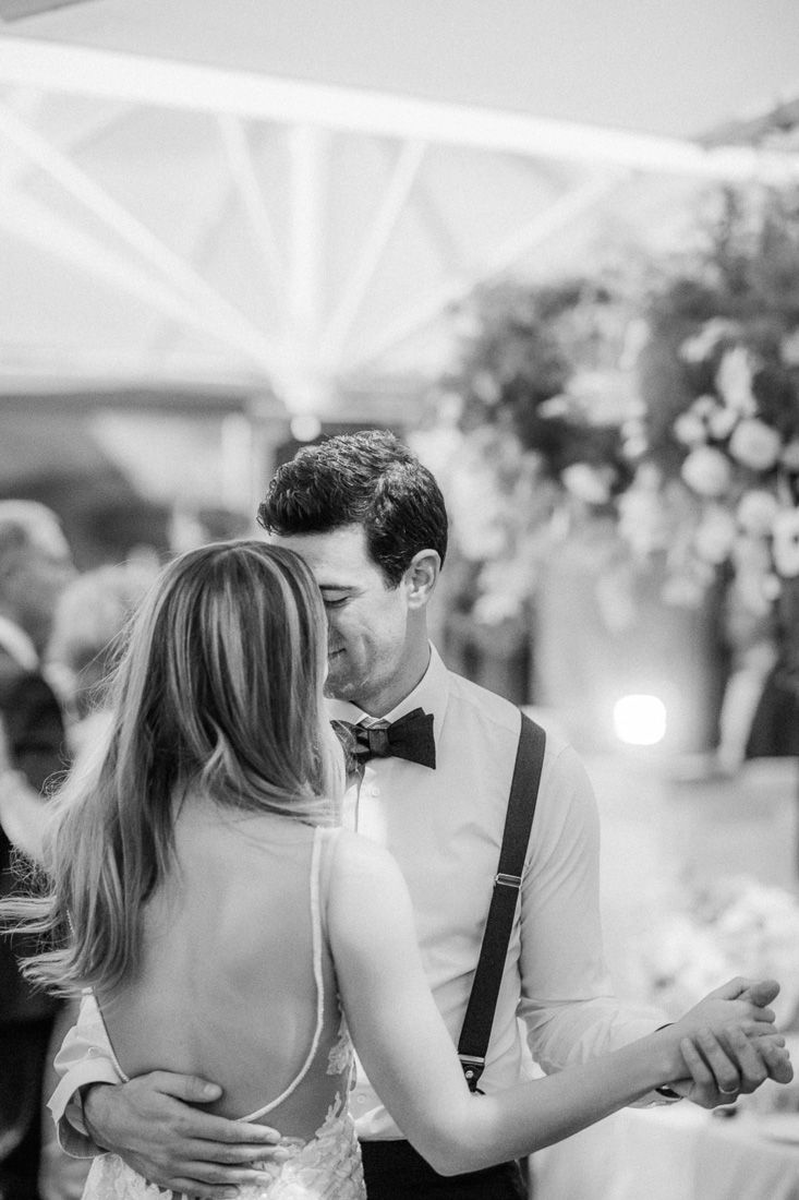 Couple dances closely under white tent during evening wedding reception.