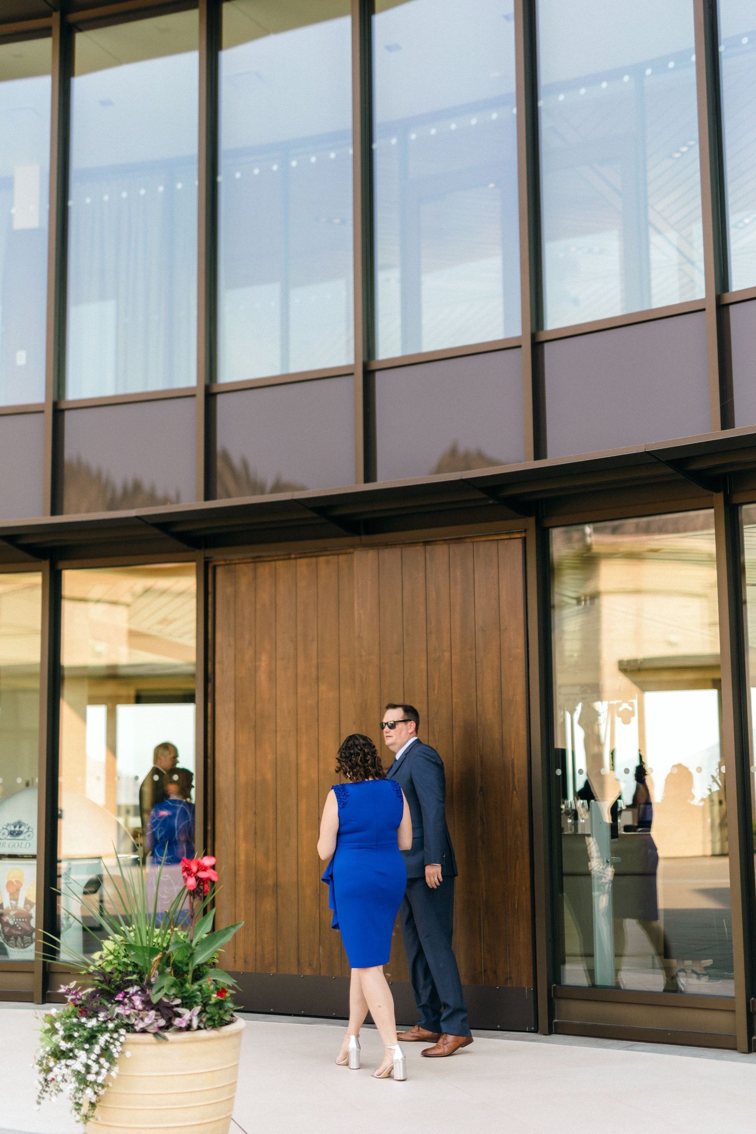 Modern glass-fronted building with wood paneling and flowering plants at the entrance.
