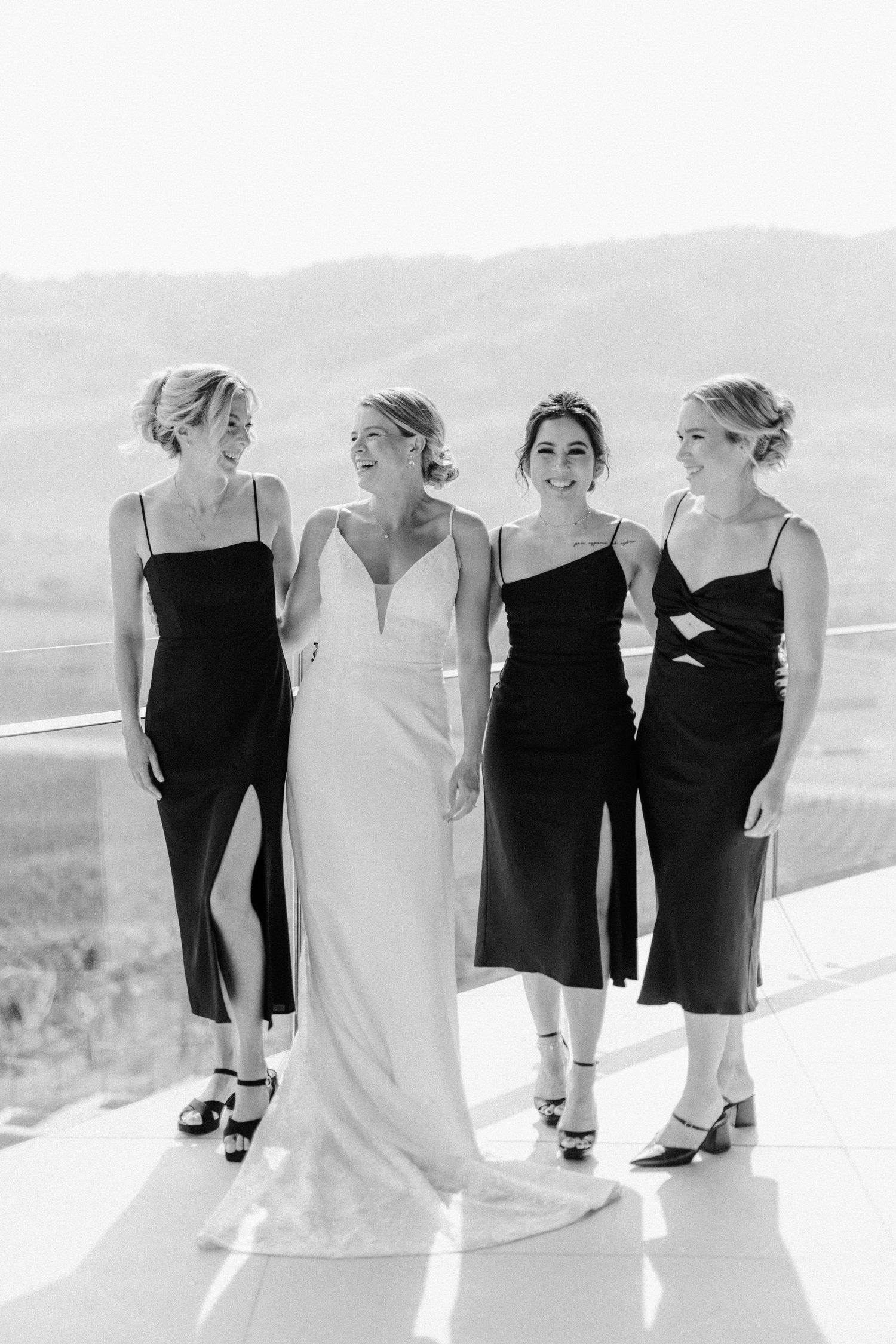 Bridal party in black and white dresses posing together on a sunny outdoor terrace.
