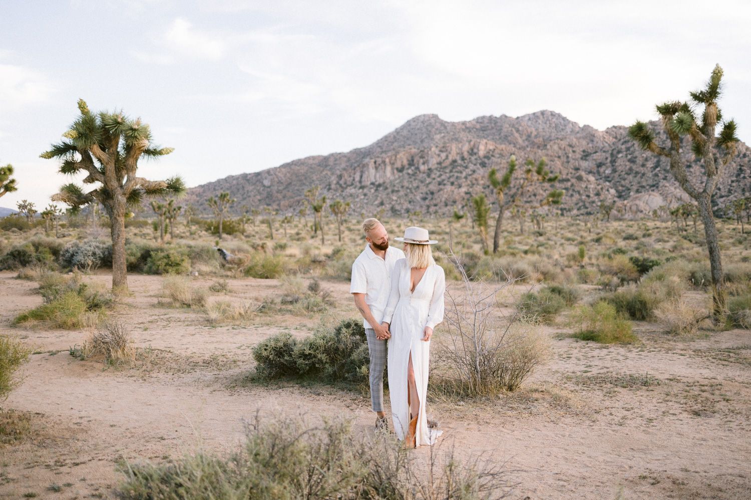 A romantic desert photoshoot featuring a couple in matching white outfits among Joshua trees.
