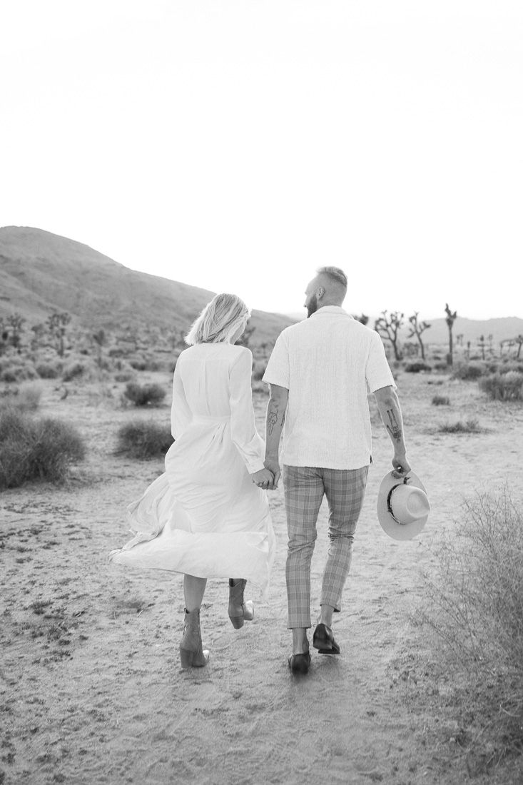 A black and white photo of a couple walking together in a desert landscape.