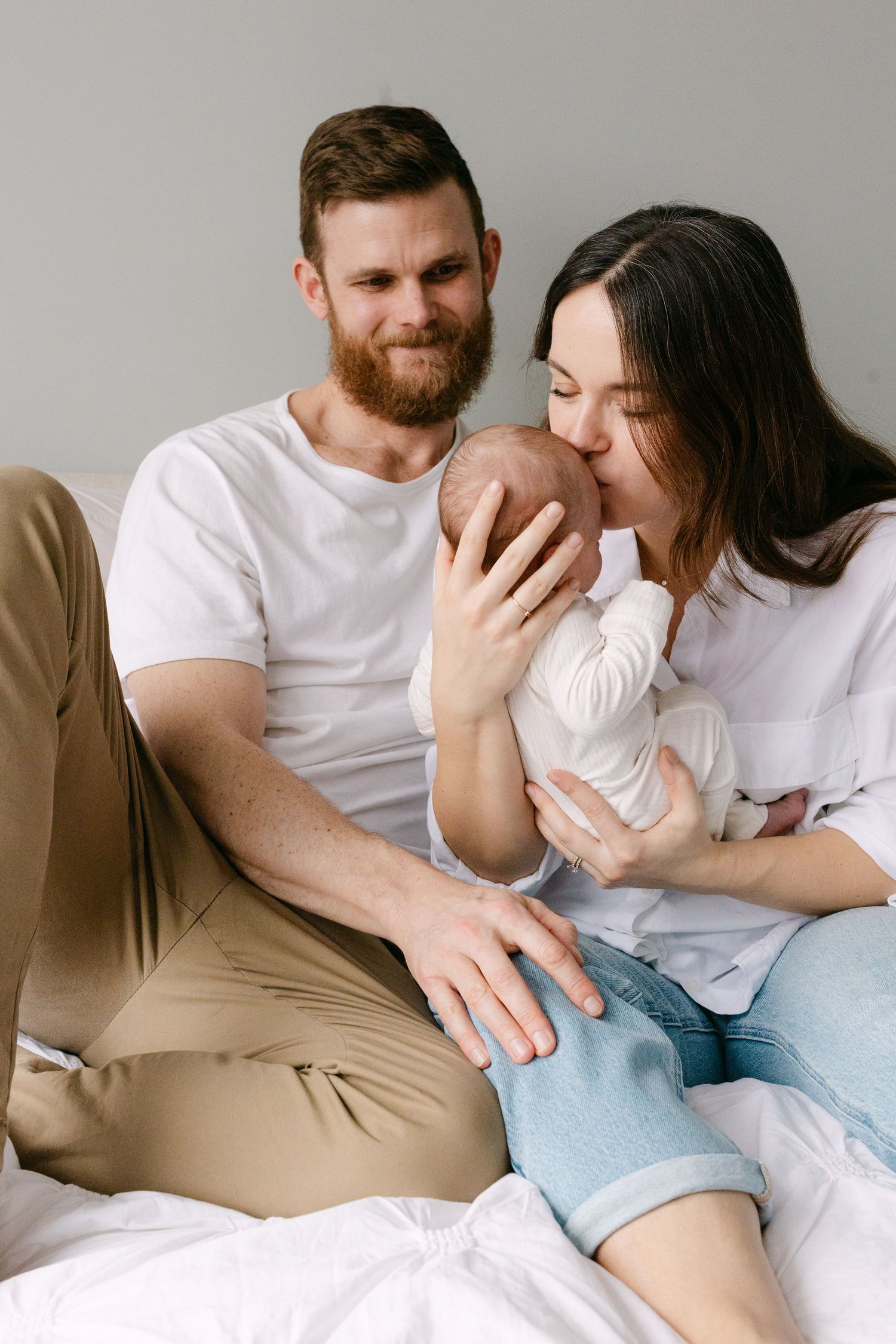A couple in white and beige clothing share tender moments together while relaxing on a couch in a series of intimate photos.