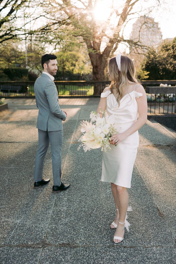 Couple in formal attire poses in a park during sunset with spring blossoms in background.