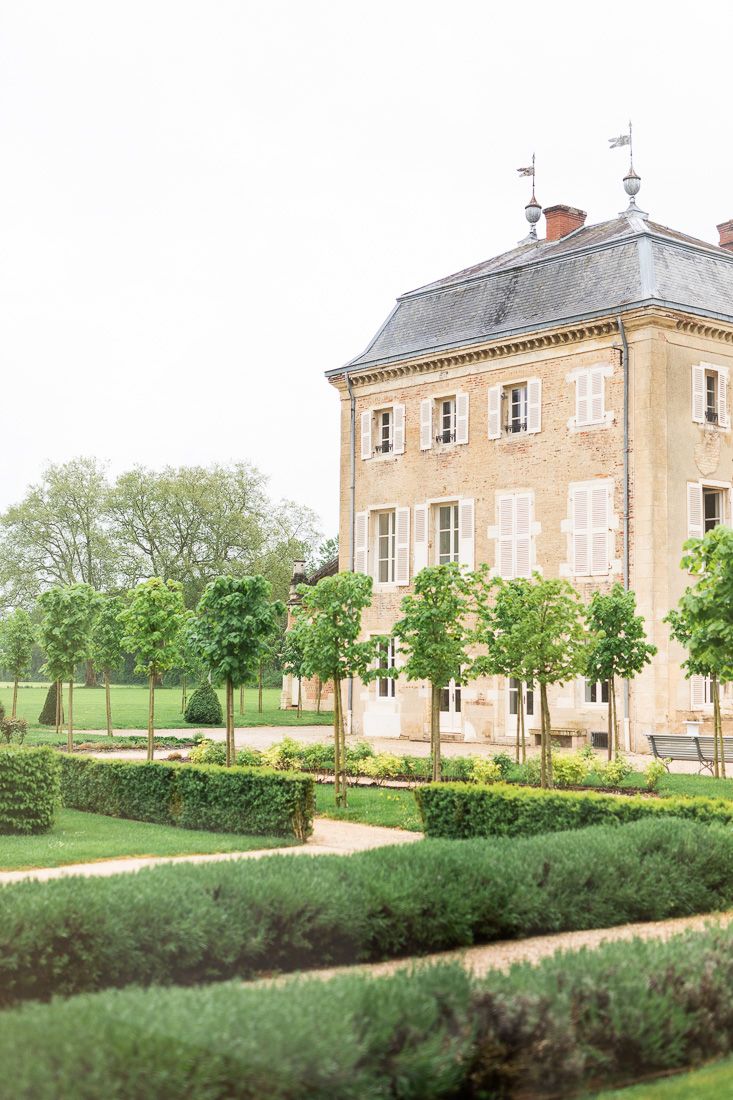 Classic French mansion with grey slate roof and formal garden featuring perfectly spaced trees.