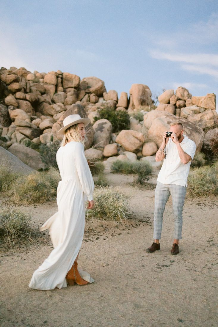 Two people take turns photographing each other in a desert setting with rocky terrain.
