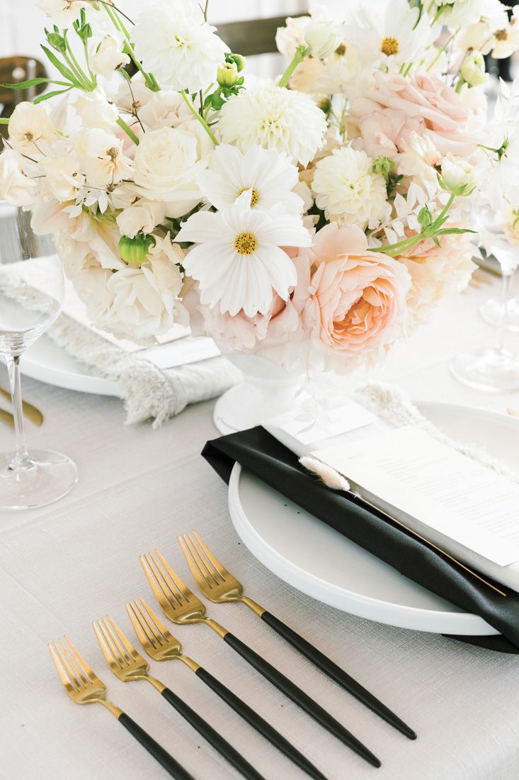 Elegant table setting with white and blush floral centerpiece and gold-accented flatware.