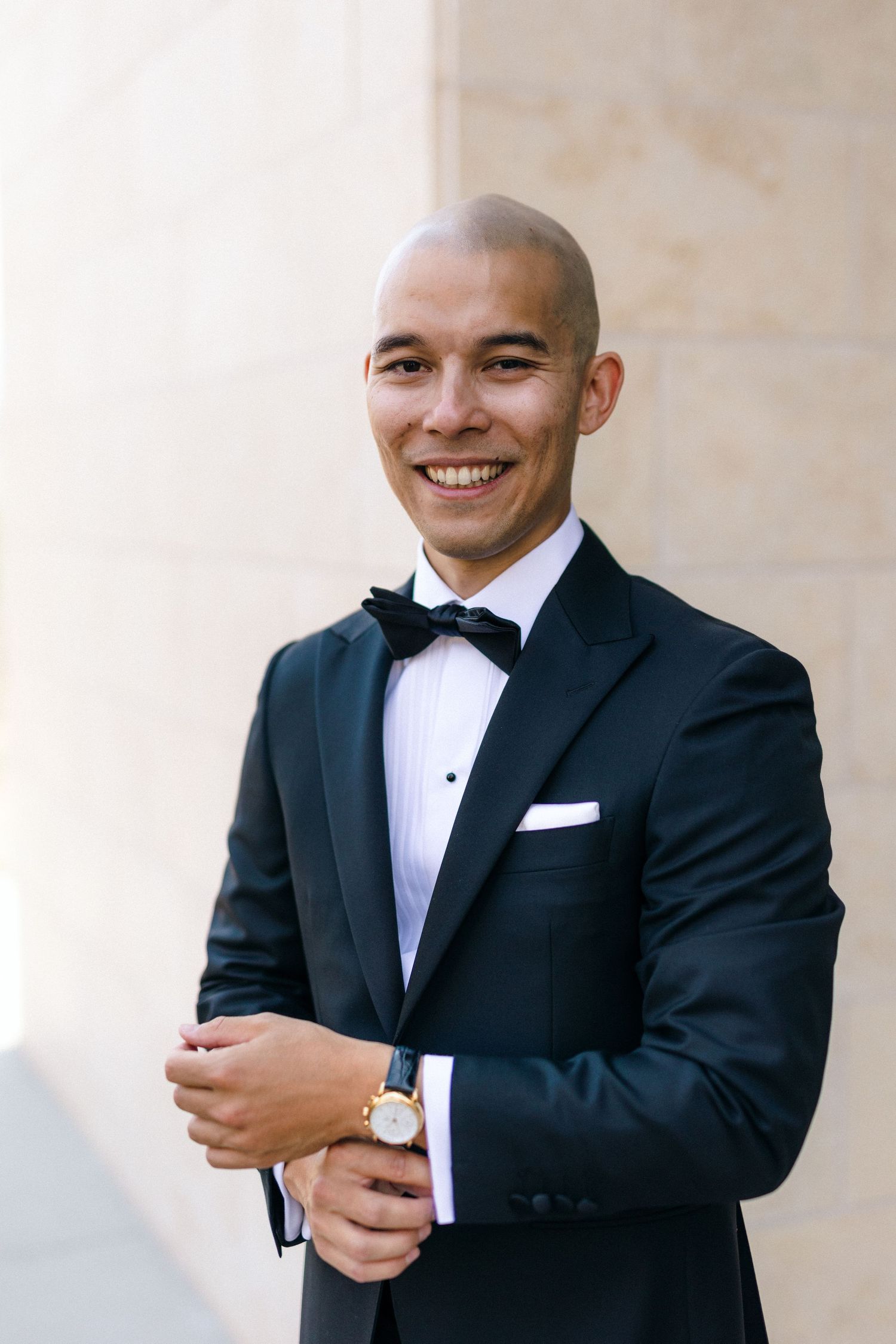 Groom adjusting his cuffs and bow tie while smiling before the wedding ceremony.