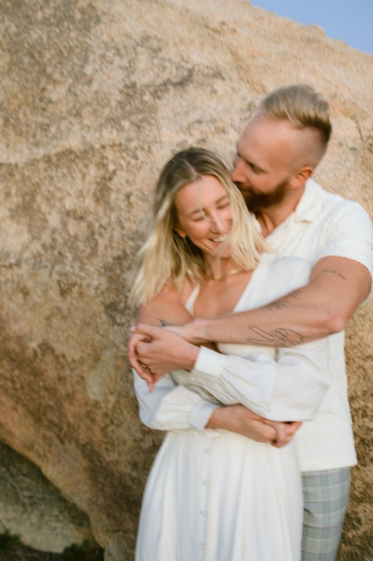 A tender embrace captured against a desert boulder backdrop.