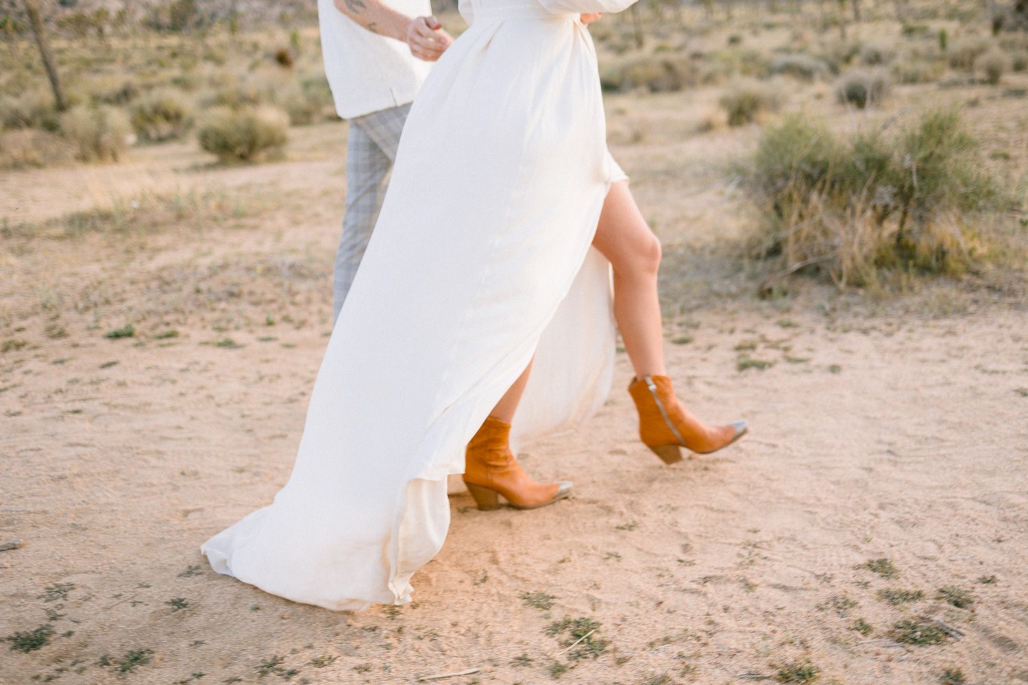 Close-up of flowing white dress and brown boots walking in desert terrain.