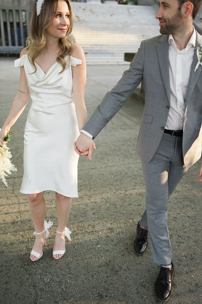 A couple holds hands while walking together, with the bride in white and groom in gray.