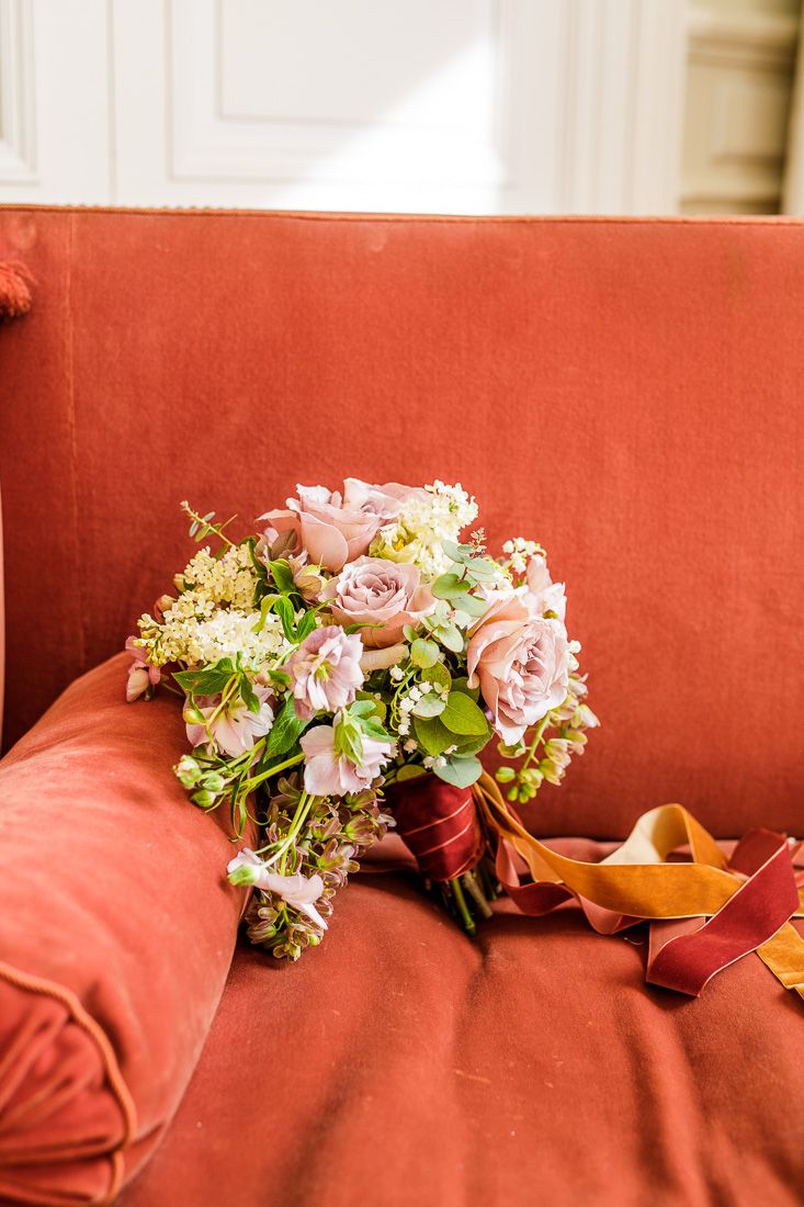 Wedding bouquet with pink roses and mixed flowers on a coral-colored couch.