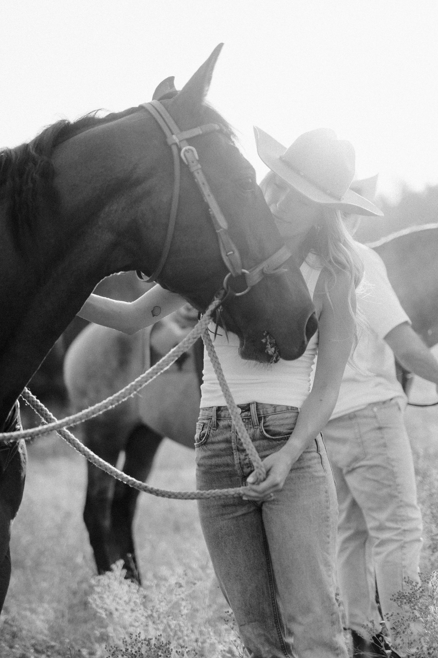 Black and white photo of a horse and Western-styled handlers in a sunny field.