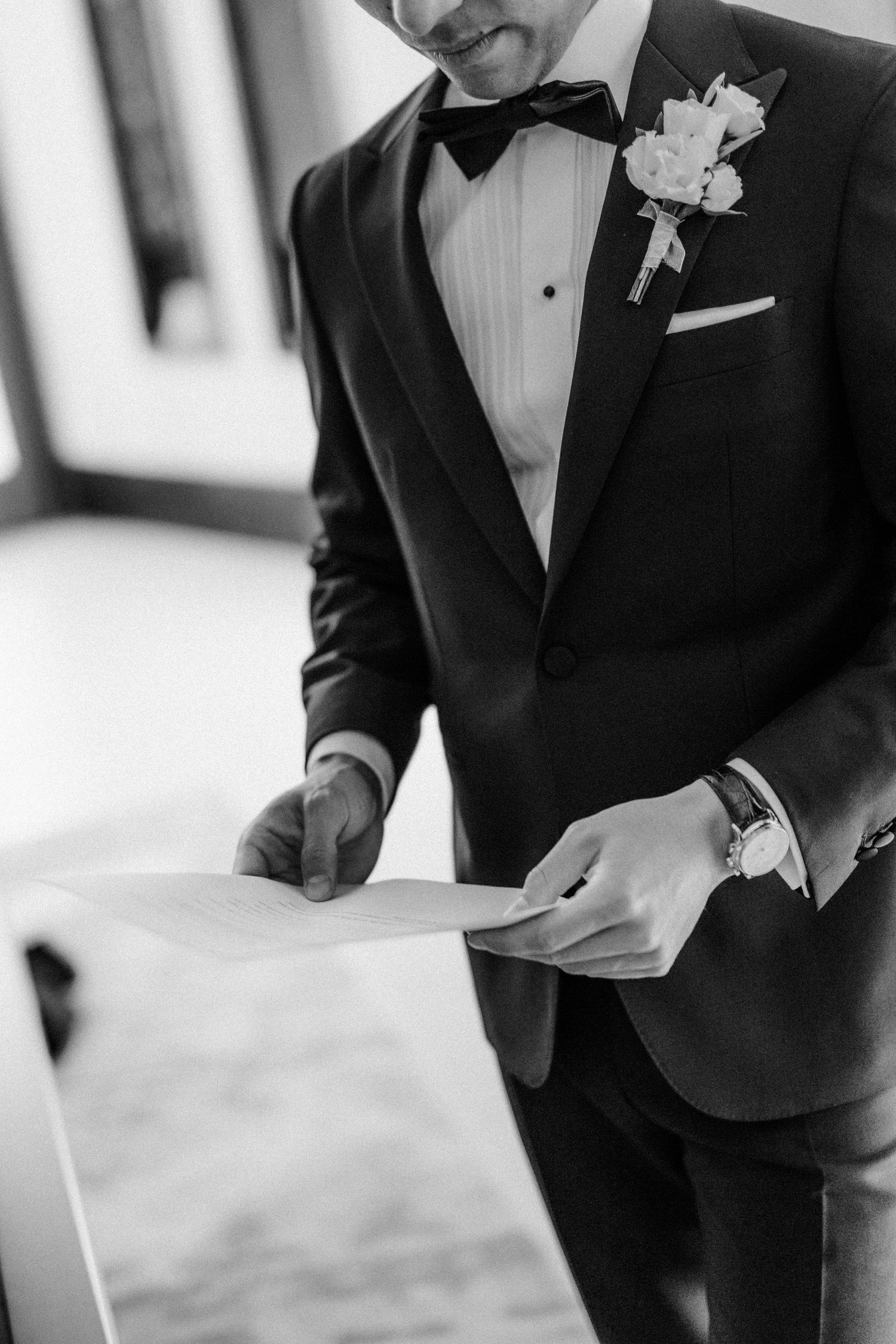 Close-up black and white detail of tuxedo with white boutonniere and bow tie.