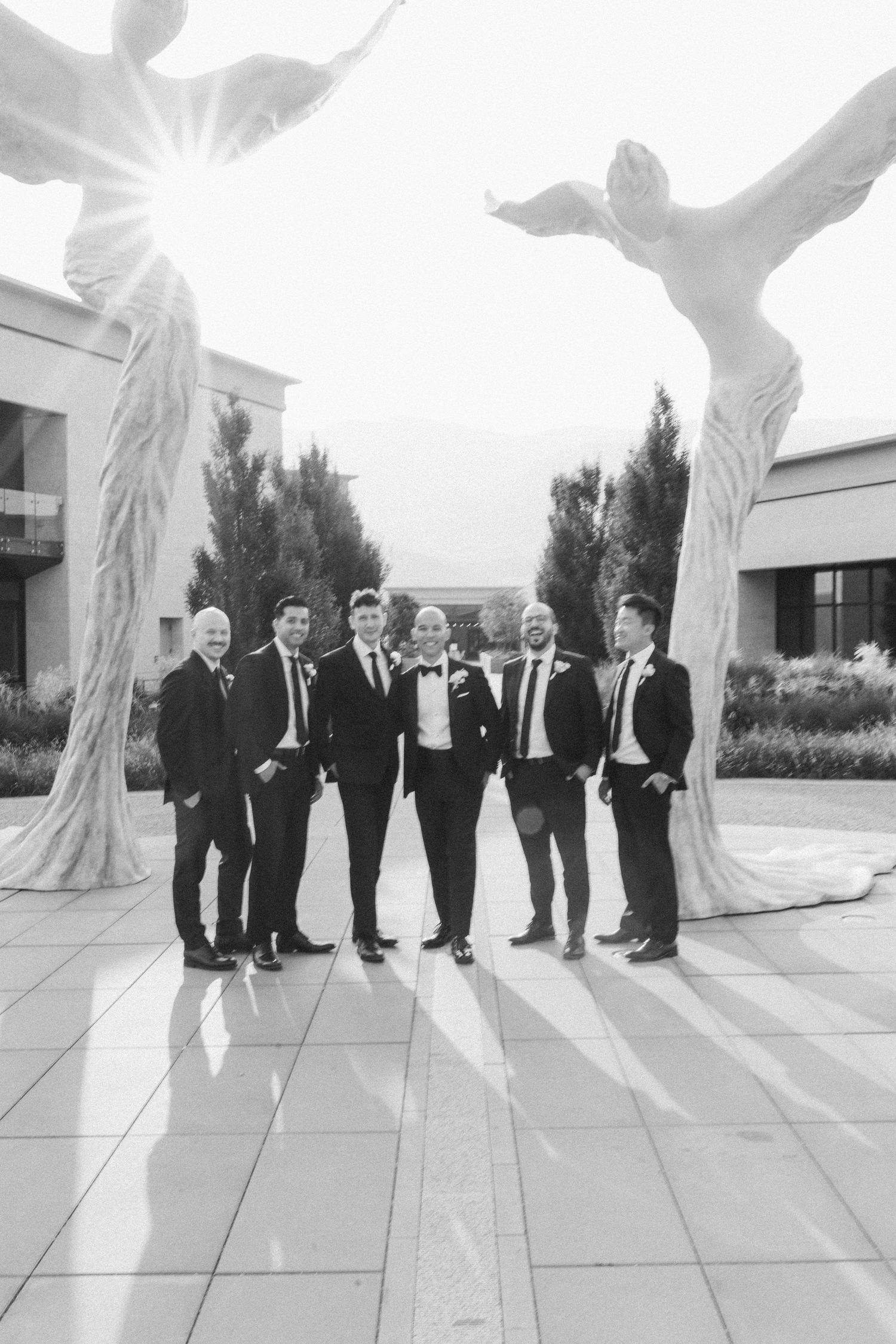 Wedding party poses between angel wing sculptures in black and white photography.