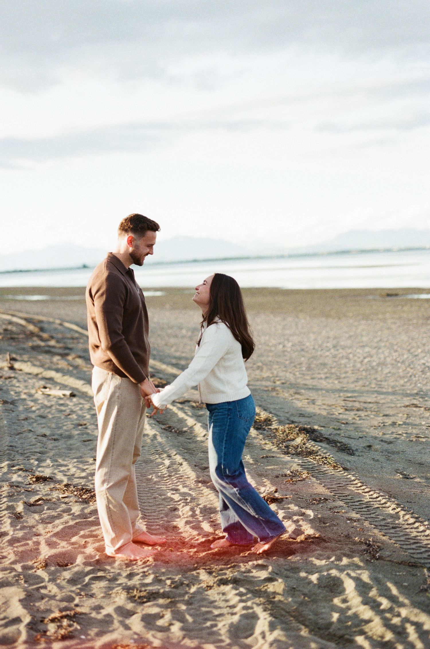 Couple dancing joyfully together on a sandy beach during golden hour sunset.