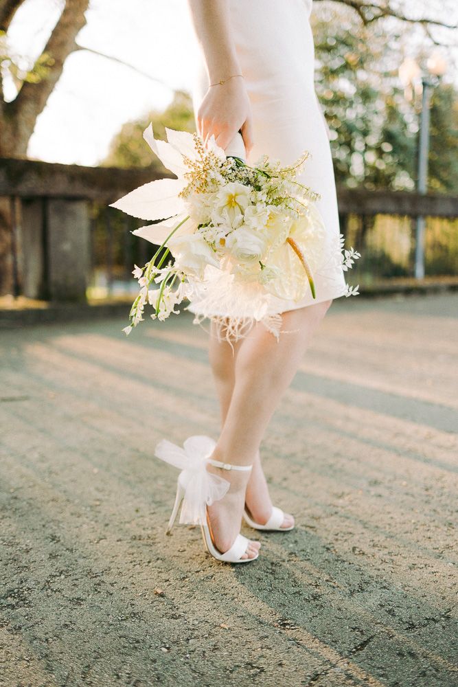 White wedding shoes and delicate floral bouquet shown against outdoor garden setting.