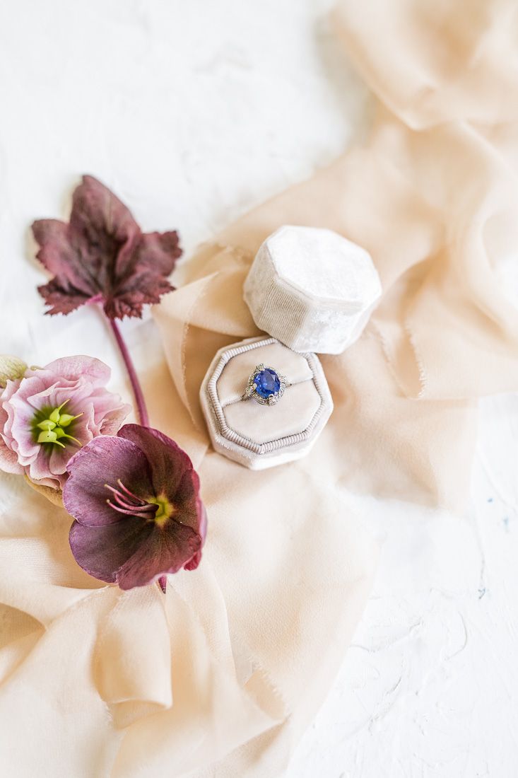 Engagement ring in white velvet box with hellebore flowers on silk fabric.