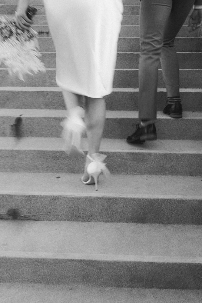 Monochrome detail of white dress and heels ascending stone steps.