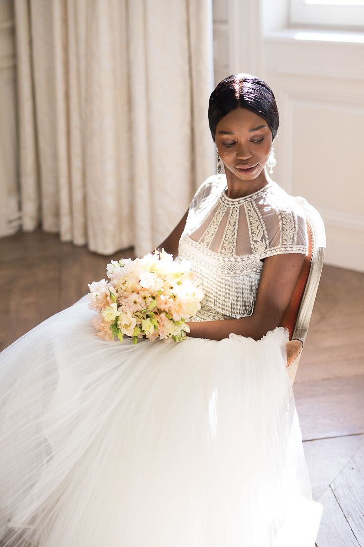 Bride in elegant high-neck wedding dress smiles while holding pastel bouquet.