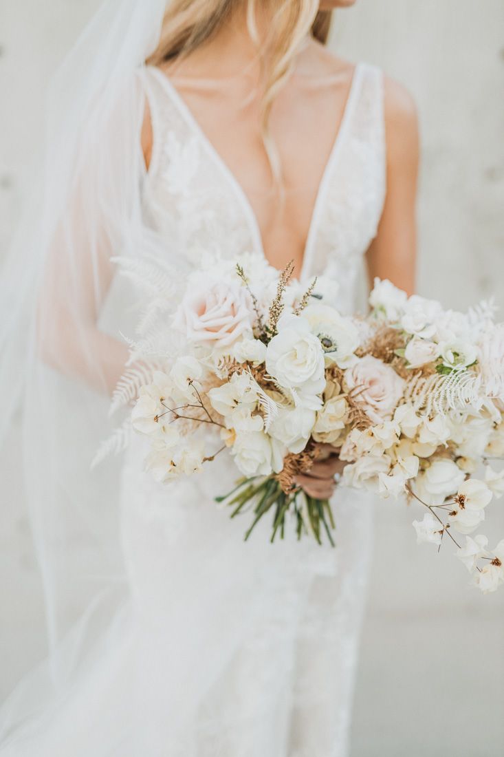 Close-up of bride holding luxurious white and blush wedding bouquet with flowing ribbons.